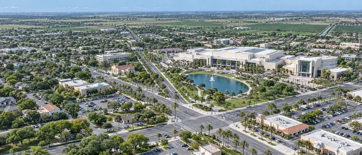 Aerial drone view of McAllen, TX with the convention center, its lake and fountain, palm-lined boulevards, and retail parking lots stretching to Valley farmland