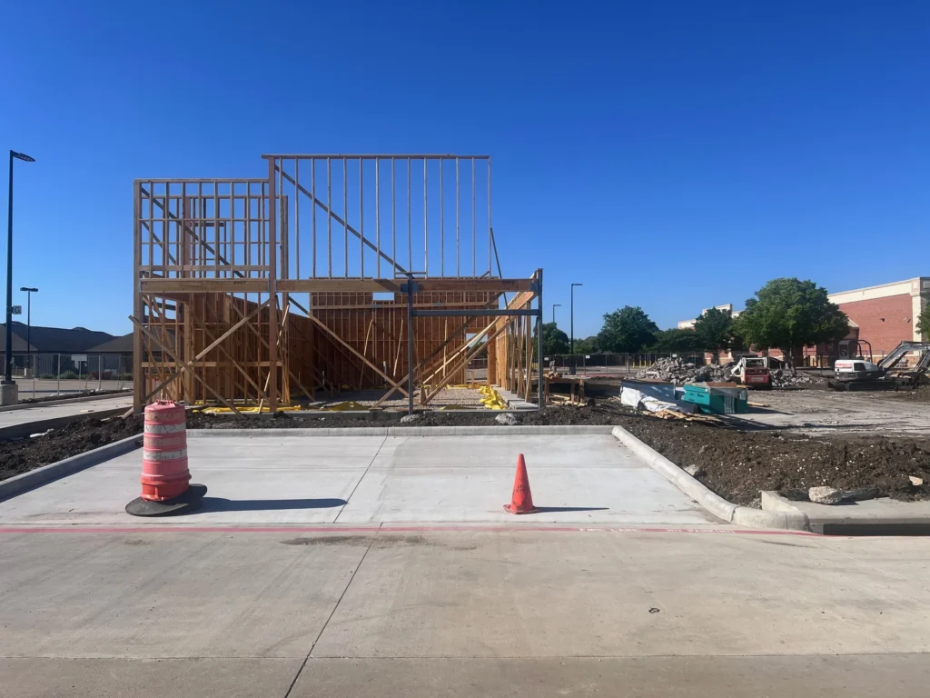 Commercial wood-framed building on a graded pad site with a clean concrete drive and a bare soil edge