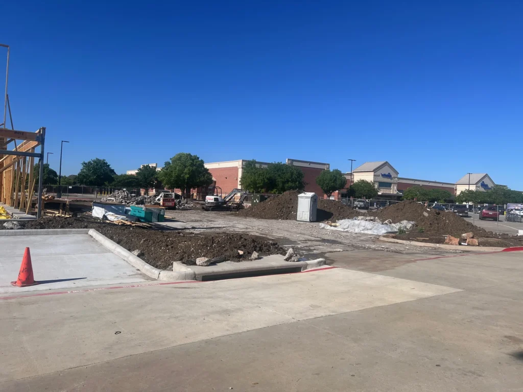 Retail pad site under construction in North Texas with bare clay soil a truck length from the finished concrete apron and street