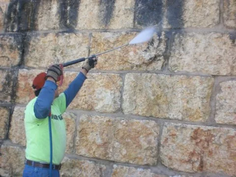 Worker power washing years of staining off a limestone block wall