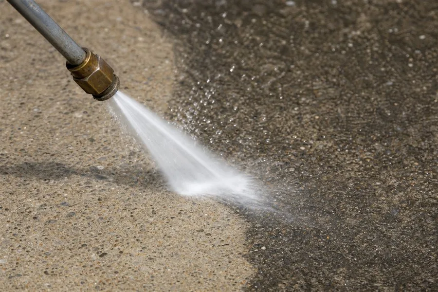 Pressure washer nozzle cutting a clean line through grime on concrete