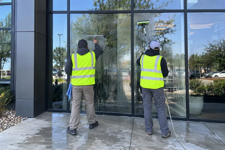 Two Moore Clean crew members cleaning a commercial building entrance with squeegee and pole brush